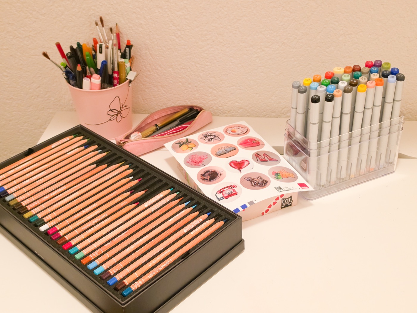 Arbeitsplatz im Atelier: Farbstiftbox, Pinselbecher, Marker und ein Bogen mit Motiv-Stickern
